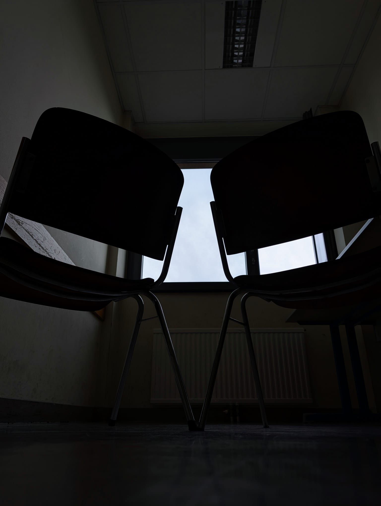 Two random backfacing chairs, hard contrast and many shadows, dark picture